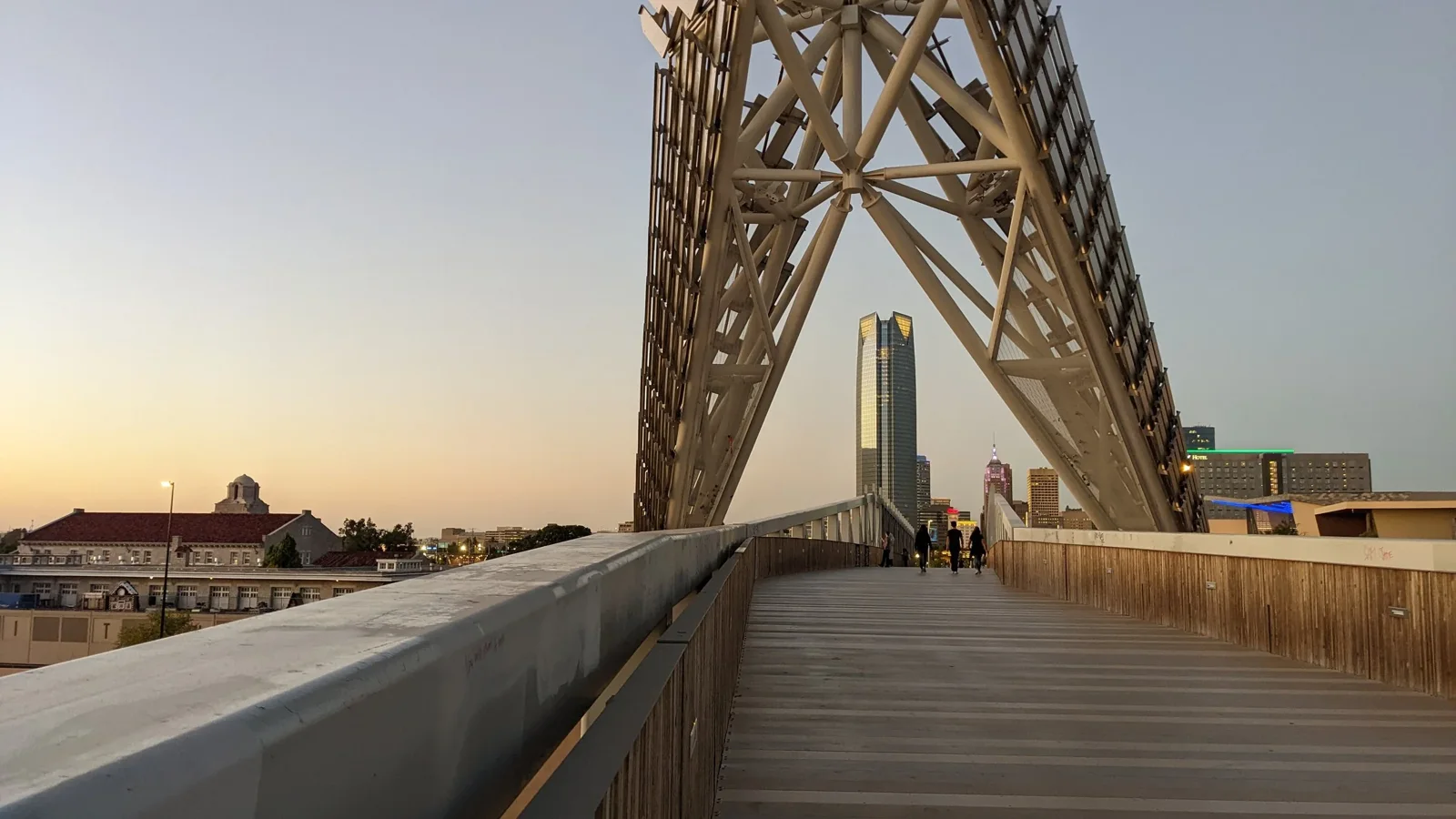 A steel bridge frames a city skyline beneath a warm evening sky.