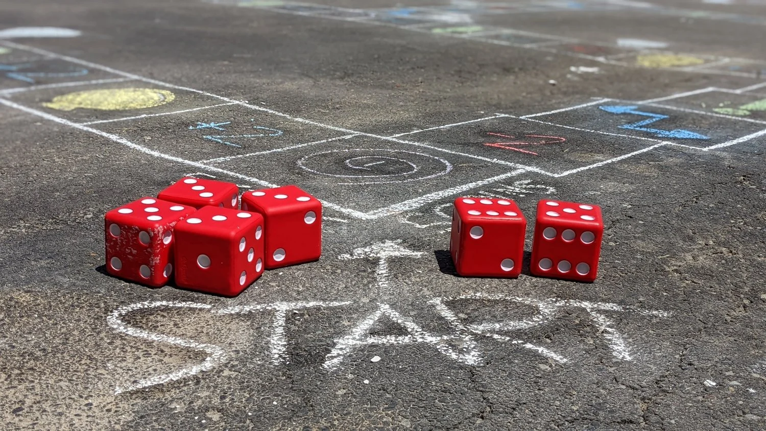 Red dice arranged on a chalk-drawn outdoor game board.