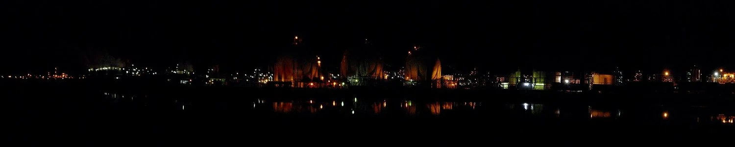 A wide nighttime waterfront scene with bright lights reflected in the water.