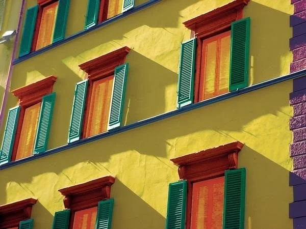 Colorful yellow building facade with red-trimmed windows and green shutters.